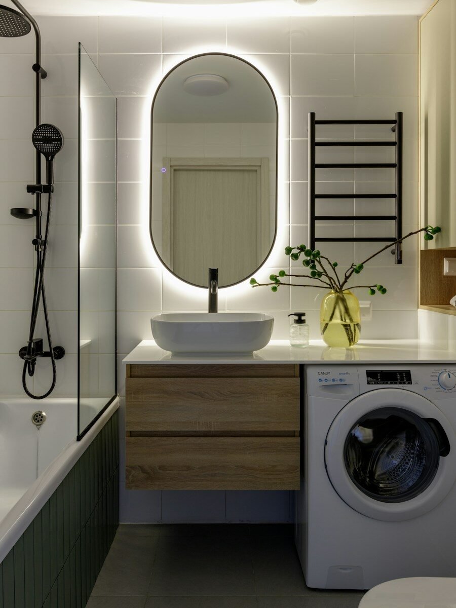 Modern bathroom with backlit mirror, washing machine, and bathtub